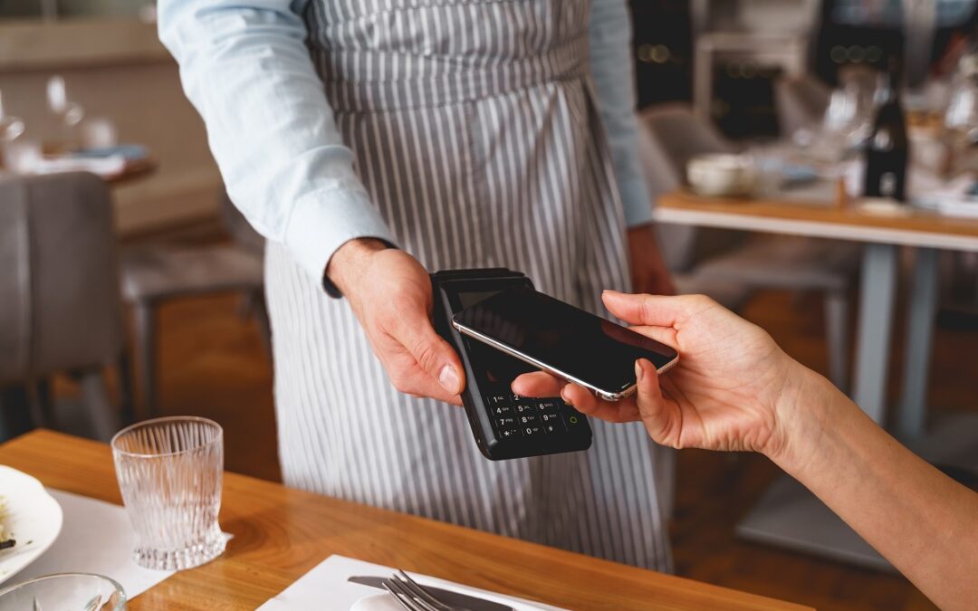 Close up of waiter holding terminal for Pay-at-the-table contactless payment and accepting payment from customer on cellphone